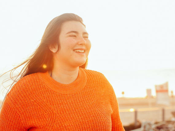 A woman stands on a rooftop at sunset and smiles. 