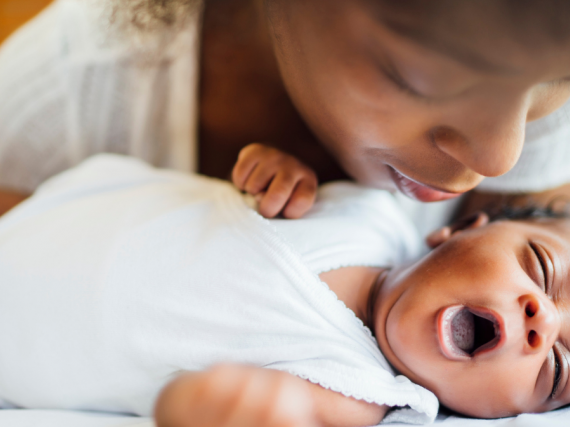 A Black mother kisses her newborn's head while the baby yawns. 