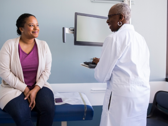 Two Black women, one a provider and one a patient, greet one another at the start of a health care visit. 