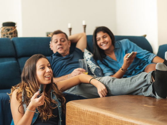 A family of three sits on the sofa and debates what to watch on TV. 