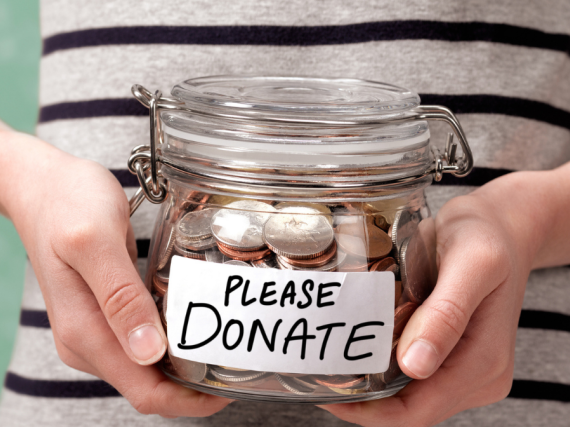 A pair of hands holding a jar filled with change and a label that says, "Please Donate."