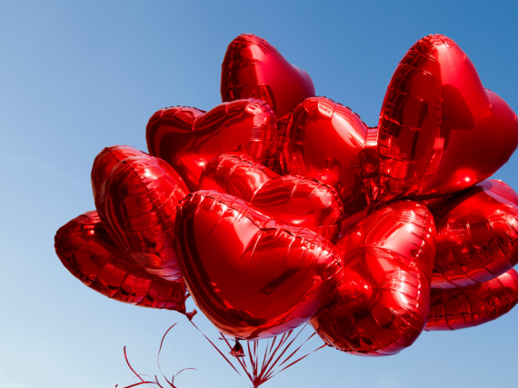 A large bunch of heart balloons against a bright blue sky. 