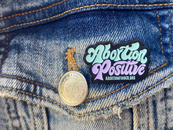 A pin on a jean jacket that reads, "Abortion Finder abortionfinder.org."