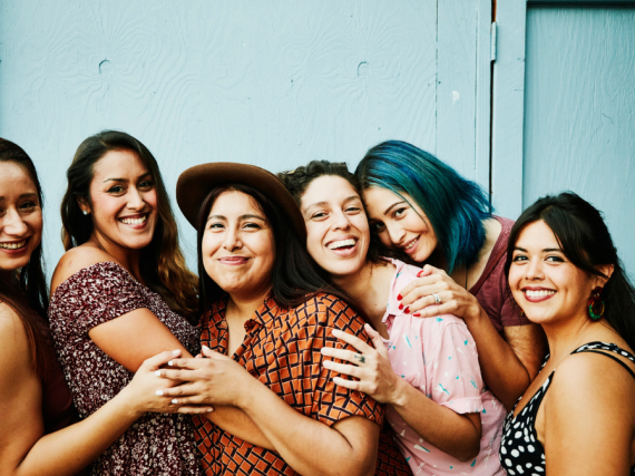 Six smiling Latina women hug. 
