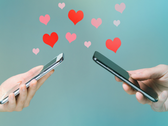 Two hands holding cell phones with hearts flowing between them.