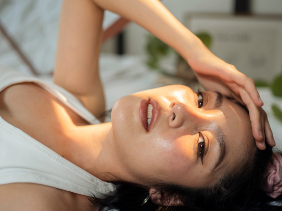An Asian woman lays down with a hand shading her eyes from the sun.