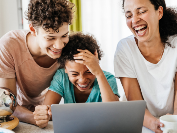 A mom and her two kids laugh while looking at a computer. 