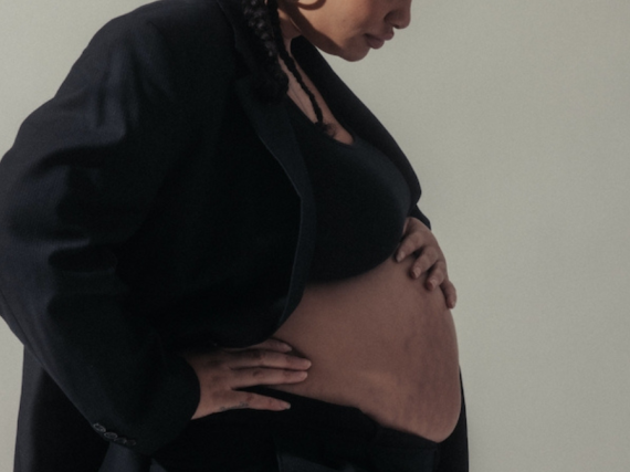 A close up photo of a Black, pregnant woman studying her belly.