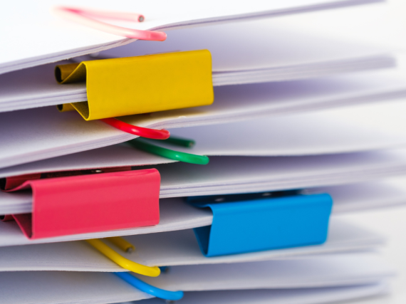 A photo of a stack of papers held together in bundles with paper and binder clips. 