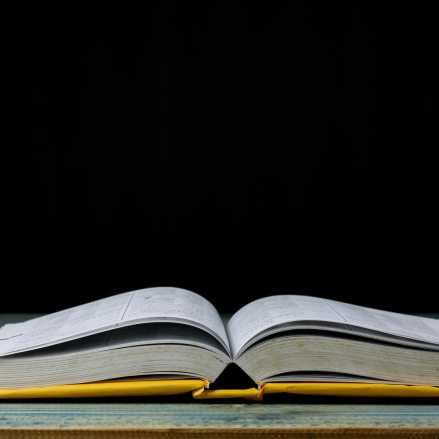 A book with a yellow cover lays open on a table with a black background. 