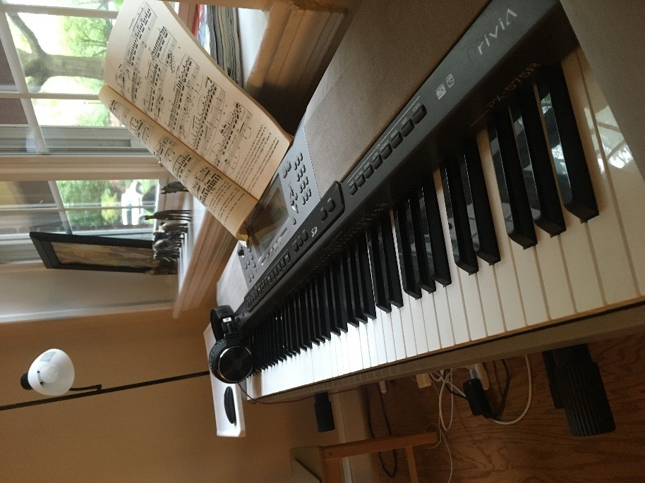 A piano next to a window with sheet music ready to play